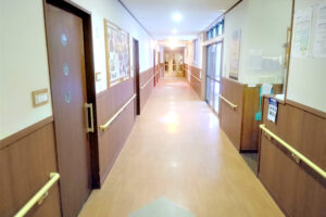 廊下・通路。両側に居室のドアと掲示板があり、明るく清潔な雰囲気